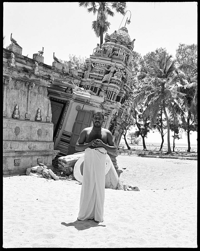 a man stands in the sand in front of a leaning temple in Sri Lanka