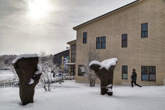 a pair of corten steel sculptures that appear to spring out of the ground, surrounded by snow with a large building in the background