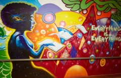 wall painted with many bright colors and featuring a woman reading in the foreground as the pages of her book fly away toward text that says "Everything is Everything"