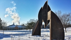 a large curvilinear corten steel sculpture in the snow against a bright blue sky with cold steam in the background