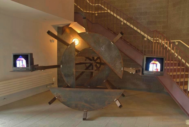 a sculpture made of steel and tv monitors in a stairwell