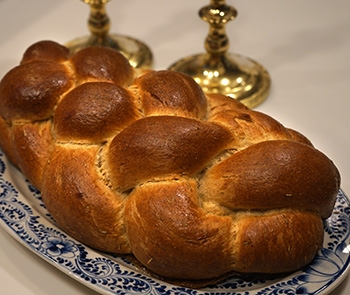 A loaf of Challah on a plate with candlesticks in background.