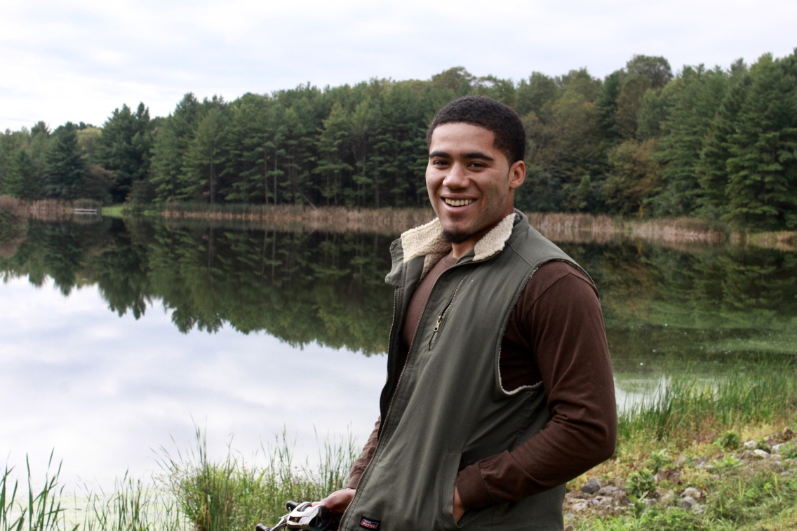 LeeCharles McNeil smiles at the camera in front of a pond and lush green trees.