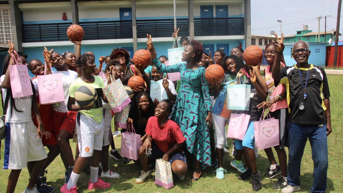 A group of smiling high schoolers pose with basketballs, colorful bags, and their teachers