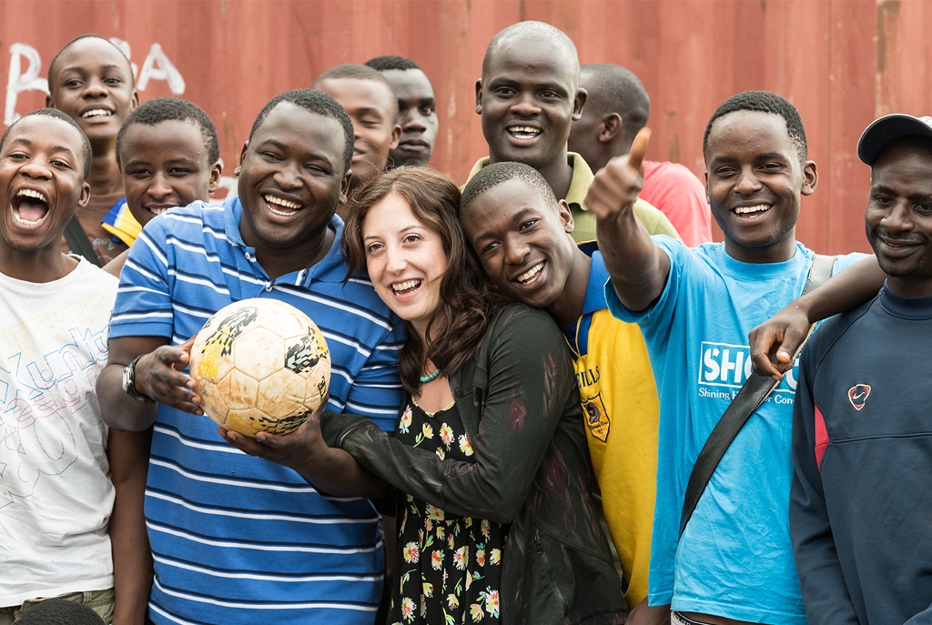 Kennedy Odede and Jessica Posner pose for the camera holding a soccer ball surrounded by smiling young men