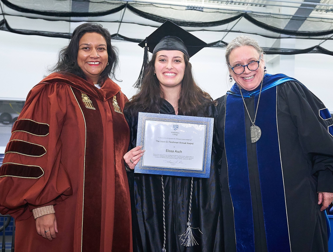 Elissa Asch, wearing a black cap and gown, poses between Smita Ruzicka and Laurie L. Patton, both in graduate hoods, with her Jason B. Fleishman award certificate.
