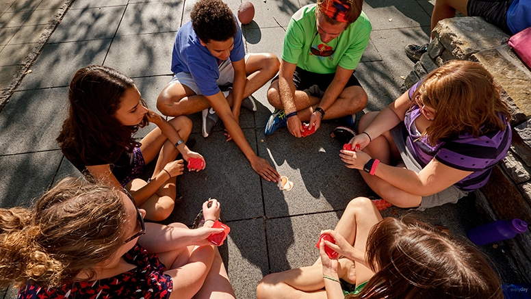 Middlebury College students and children sit outside playing cards.
