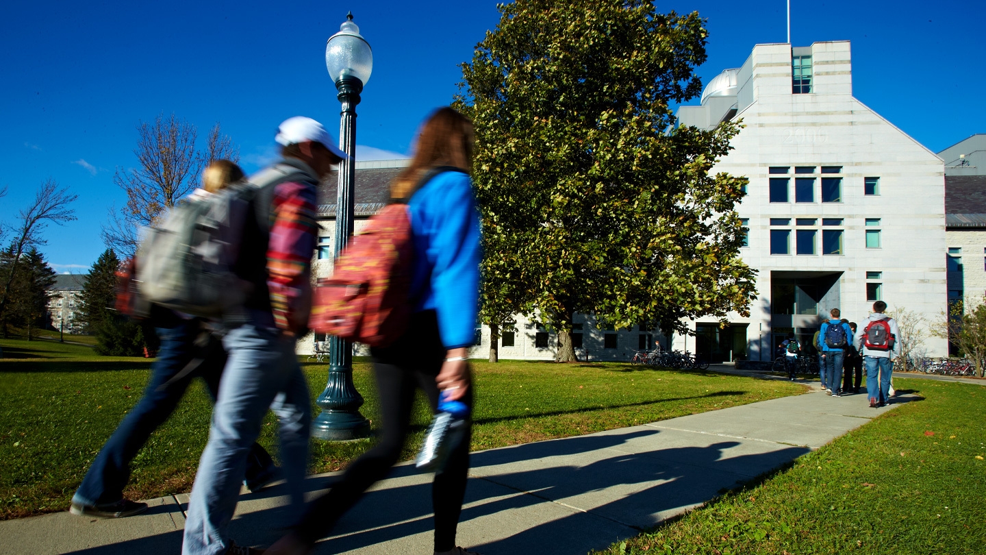 Student walking on campus beneath a bright blue fall sky.