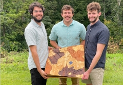 Three men holding a wooden carving of a map