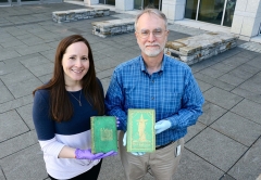 Jody Smith and Joseph-Watson holding green books outside Davis Family Library