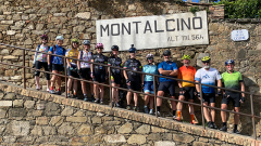 group of about a dozen cyclists standing on a ramp by a sign for "Montalcino"