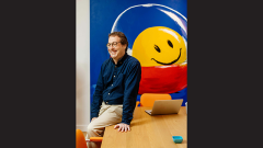 Ken Carlton in front of a red, yellow, and blue mural of a smiley face