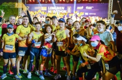 A group of runners at the Longbien Marathon in matching yellow shirts and various colored running shorts pose for a celebratory photo