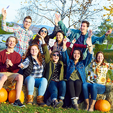 A group of Midd students posing happily with pumpkins outside on a fall day during Homecoming weekend.