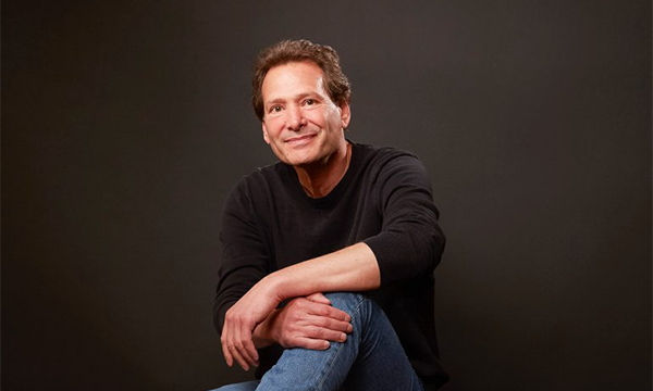 Dan Schulman in black sweater and jeans against a black backdrop