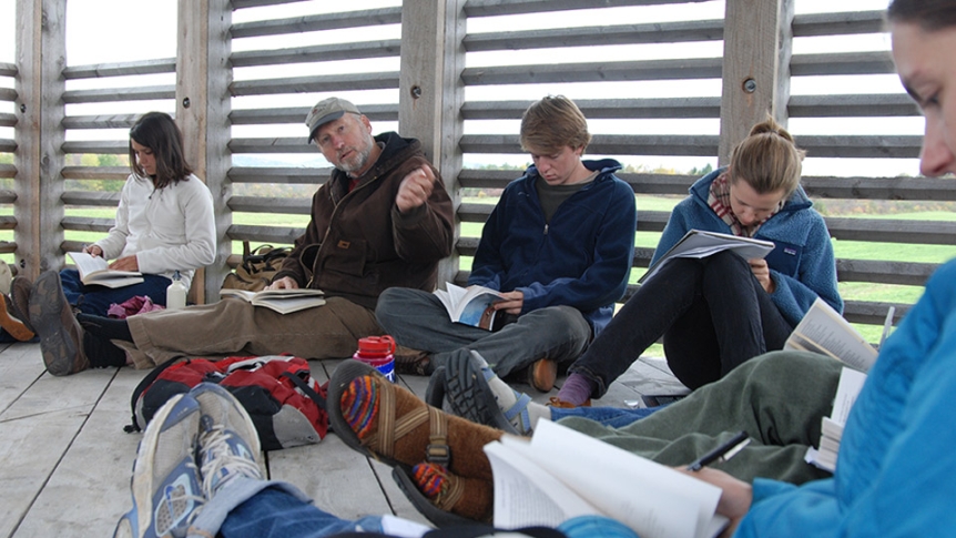 A faculty member meets with students in an outdoor shelter to discuss a nature reading.