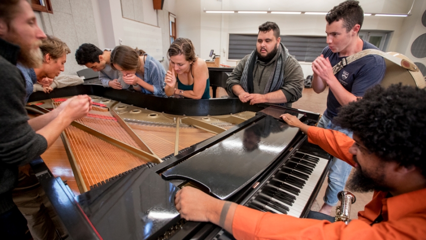 Students work with a music professor around a piano. 