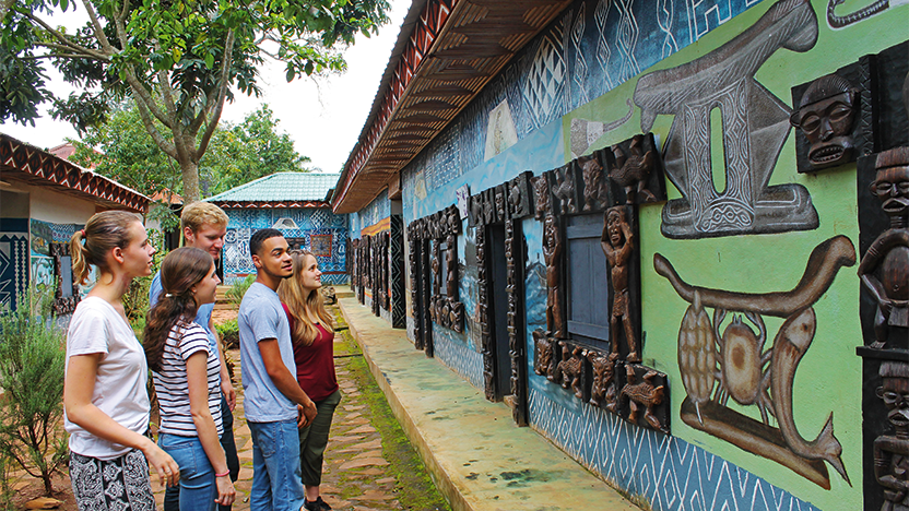 a group of students examining an elaborately decorated building in the Cameroonian village of Batoufam