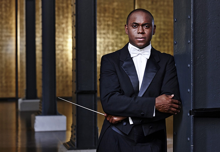Portrait of Kazem Abdullah who is wearing a tuxedo and holding a conductor’s baton