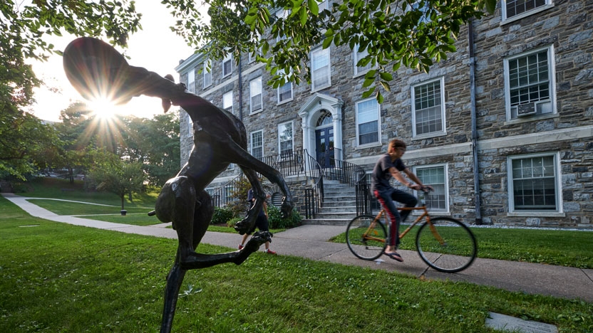 A student rides his bike past the Frisbee dog sculpture on campus.