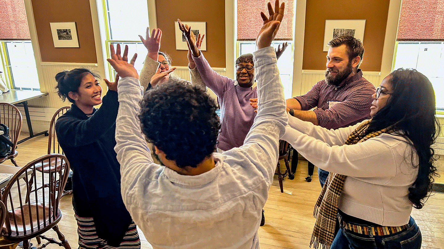 Five teachers stand in a circle with arms uplifted. 