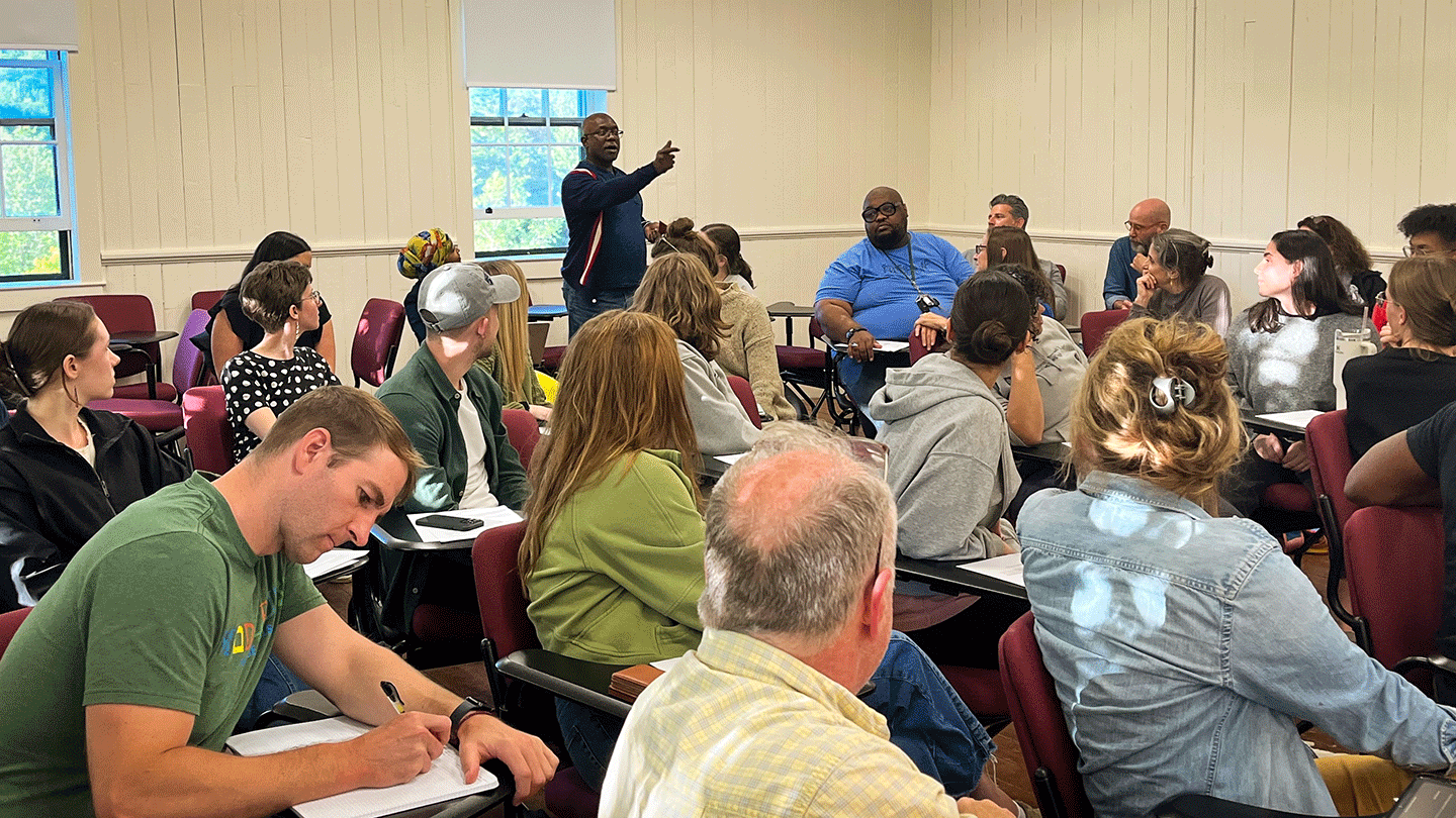 A classroom full of educators turns to look at a speaker who stands to share.