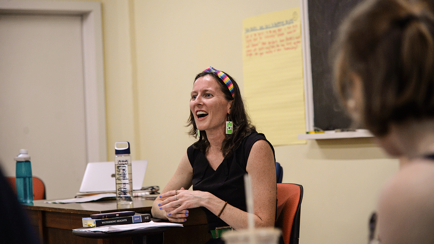 A woman smiles as she speaks in a classroom while another looks on attentively.