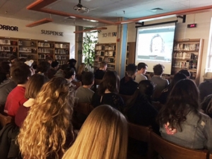 Students listen to video feed of teacher speaking in classroom.