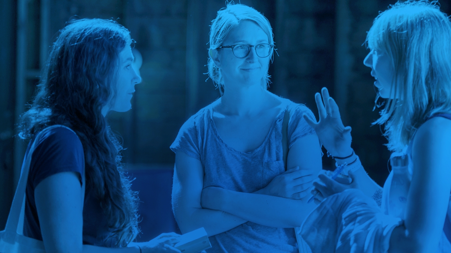 Blue tinted image of three students talking in the barn.