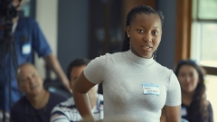 A female student stands, preparing to speak, in a classroom setting.