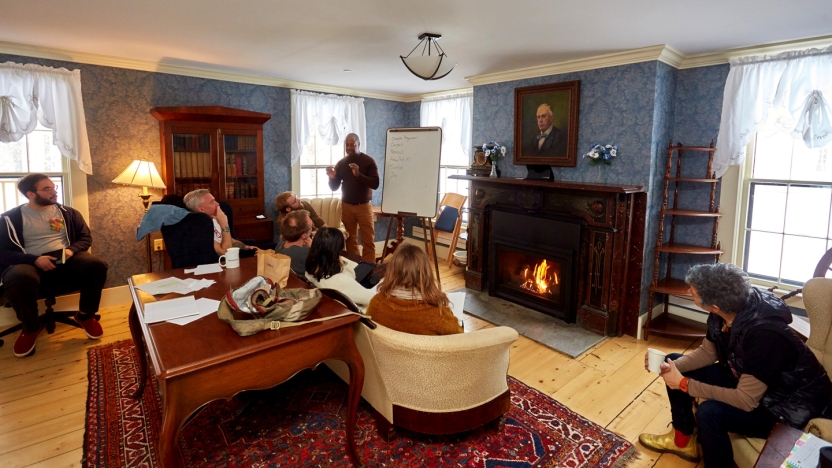 Bread Loaf School of English instructor teaching students in front of a fireplace in a campus building.