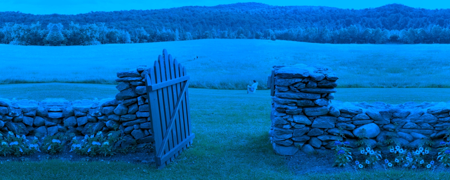 Stone fence with open wooden gate, leading to pasture. Student sitting in chair in distance.