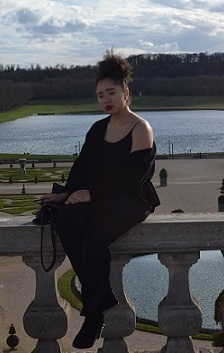 A student sits on a balcony above a fountain and gardens