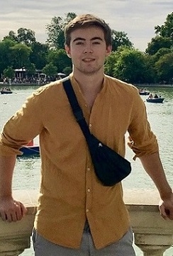 A student stands in front of a pond with boats on it