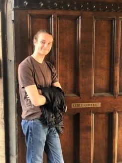 Student smiling by the door marked Keble College