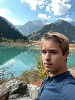Student in front of a blue green lake and mountains