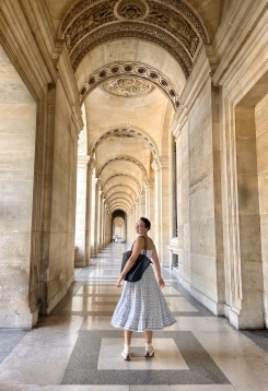 Student in a white dress turning back to look at the camera while walking down an ornate stone hallway