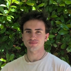 Student in a white shirt posing in front of greenery