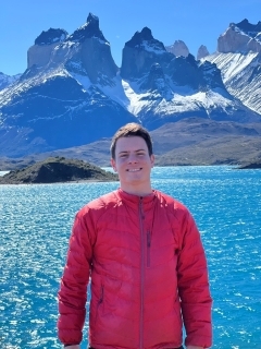 Student in a red jacket in front of blue water and mountains