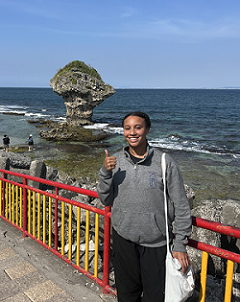 A student giving a thumbs up in front of the beach