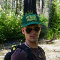 Student in a green baseball cap and sunglasses posing in a forest