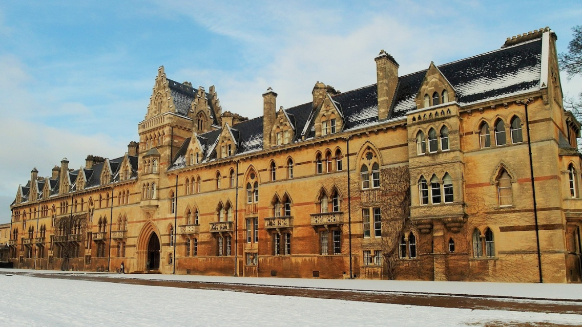 The beautiful golden stone of Christ Church College is set against a blue sky and white snow.
