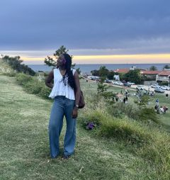 Student posing on a grassy hill by the ocean