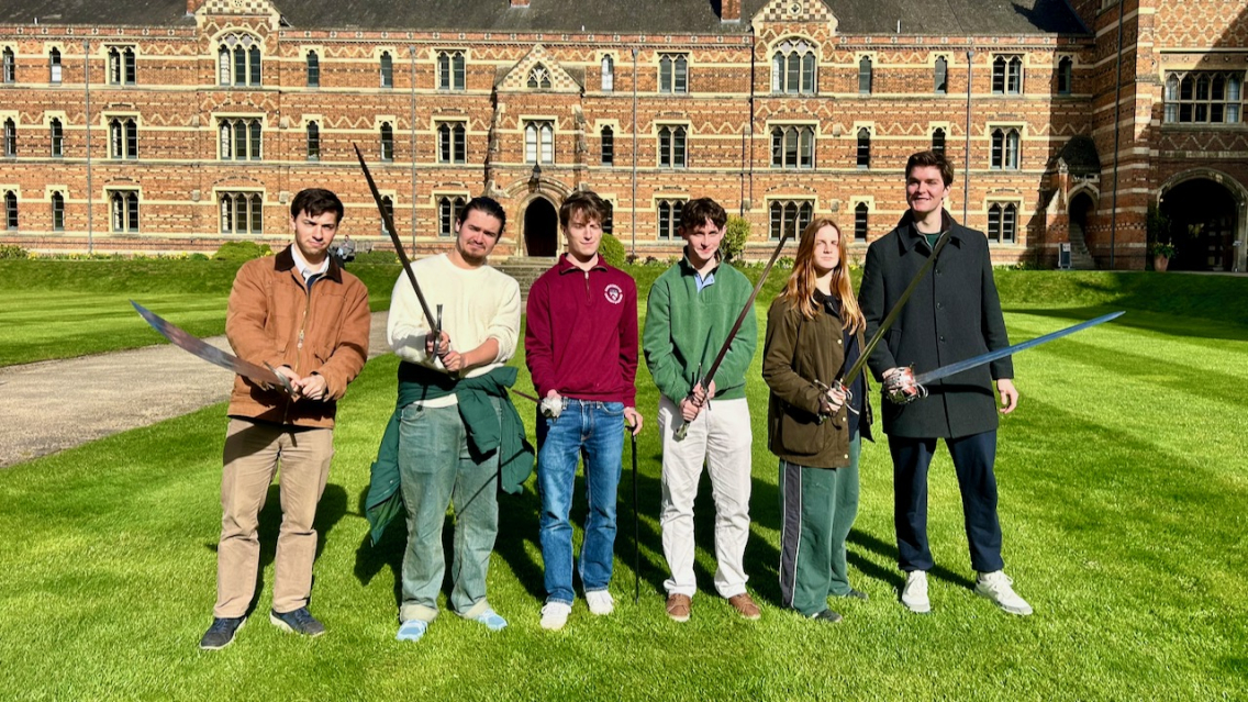 Students pose with swords in Keble College quad on a sunny day.