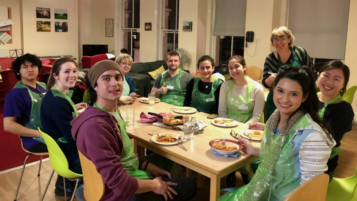 Students sit around a table in the shared kitchen for a cookery class.