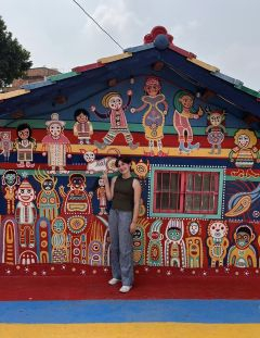 Student posing in front of a mural covered building