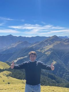 Student giving two thumbs up with mountains in the background