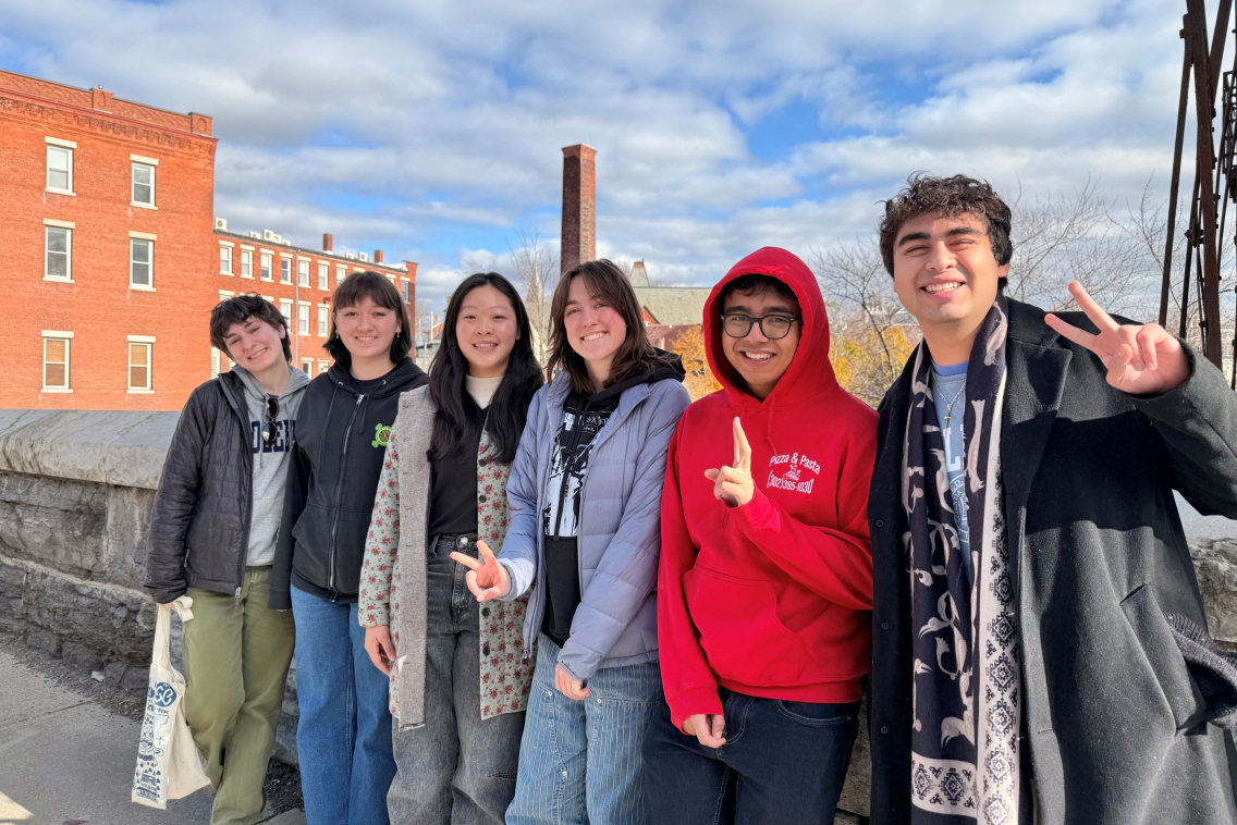 A group of six students smiling in front of brick buildings