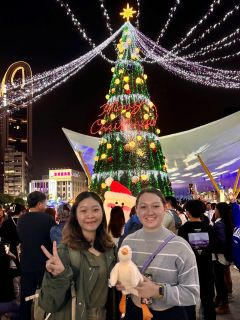 Two students smiling in front of holiday lights