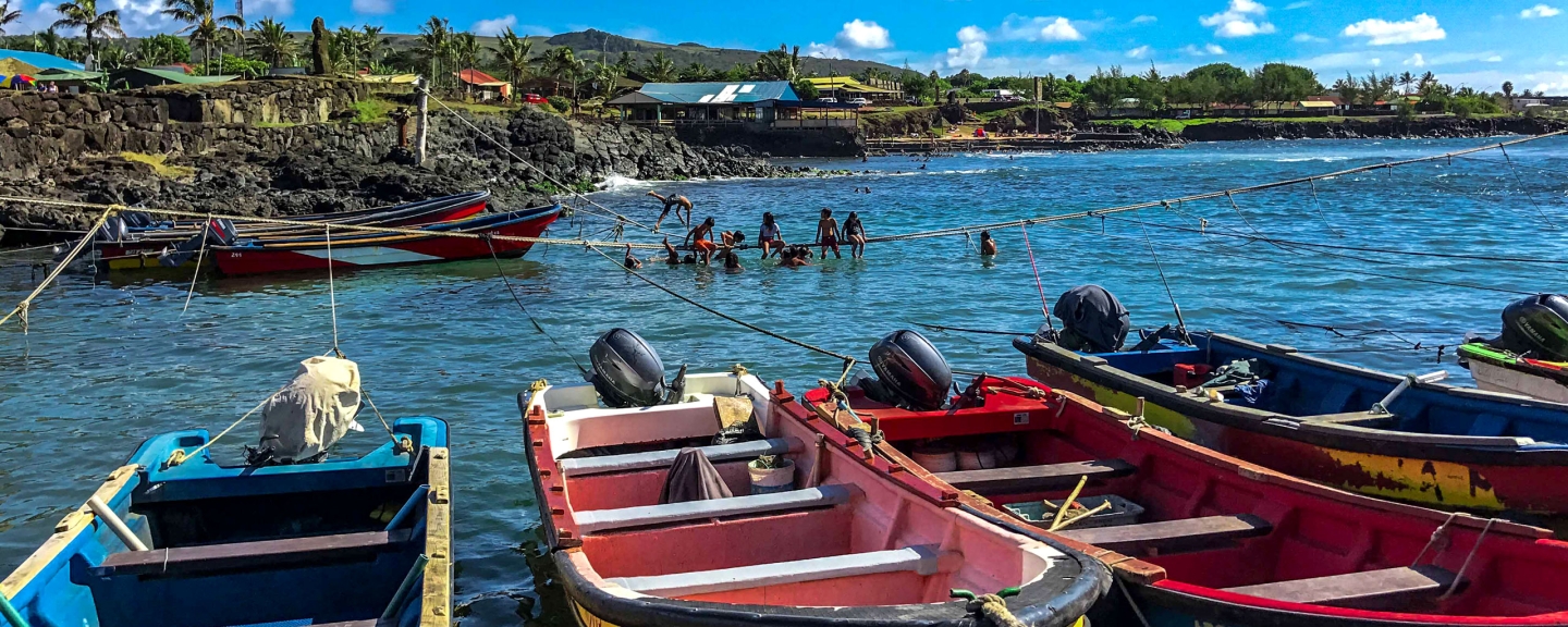 Boats on water near shore with children playing in water nearby.